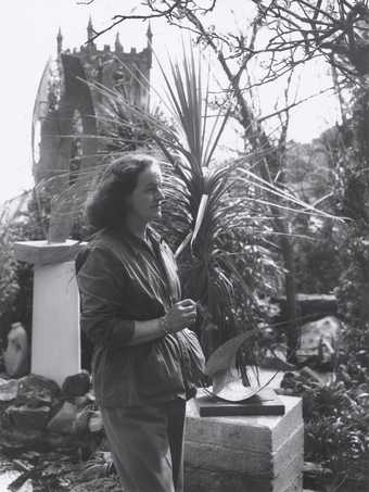 Black and white photograph of Barbara Hepworth in gardens with sculptures