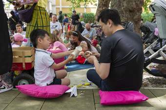 A man and a boy sitting on pink cushions make something together facing away from the camera, outside Tate Britain