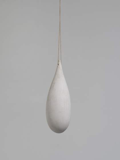 A drop-like sculpture hanging from a thin support against white backdrop