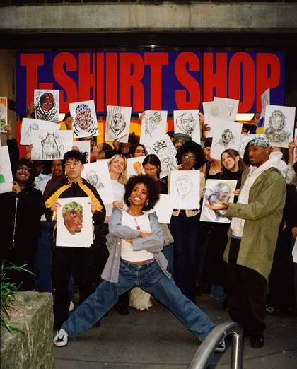 Artist Teoni standing in front of a group of people holding up painted portraits