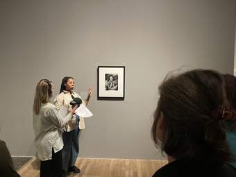 Person talking to a group of people in front of an artwork in a gallery