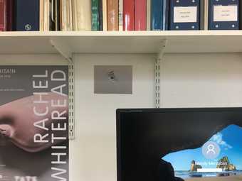 The login screen of a computer with the name 'Mandy Merzaban' (current Brooks Fellow); postcard of a hole in plaster, a Rachel Whiteread poster, and above a shelf of books and files