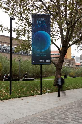 Person walking along a pavement with an advertising banner behind them for Tate Lates.