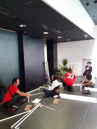 Four young people are sat on the floor putting clothes rails together