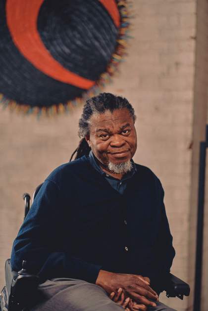 Yinka Shonibare sitting on a chair, smiling and looking at the camera