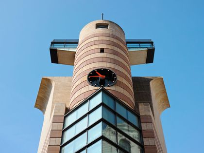 The top of a building featuring a cylindrical tower, pointed windows and a clock.