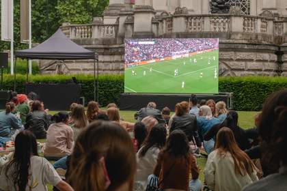 People on a lawn watching a large projector screen playing the women's Euros game