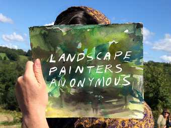 Photograph taken outside, top third of background is blue sky, bottom is green fields and trees. A face is obscured by a watercolour drawing held up in front of it with the words 'Landscape Painters Anonymous' painted on it in white.