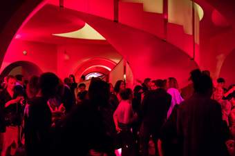 A large crowd of people dancing in a room with red lighting