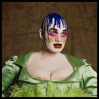 Person with bold and colourful stage makeup and a green dress