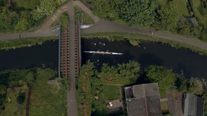 A birds-eye view of a river with a bridge and people canoeing.