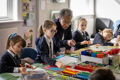 A photograph of artist Ingrid Pollard standing behind a table a children crafting