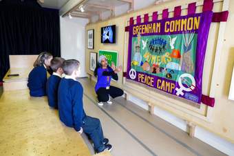 A photograph of a guide pointing at an artwork in the Mobile Museum and talking to a small group of school children