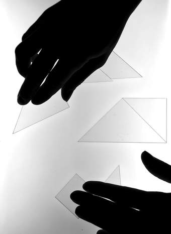 two hands in black shadow move perspex triangles on a lightbox