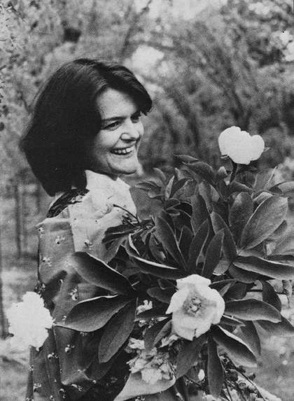 A black and white photograph of a woman who is smiling and holding some flowers and leaves.