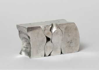 A silver sculpture, shaped like a segmented block, against a white background
