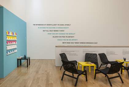 A room with several chairs and a small table with museum vinyl printed on the wall. The vinyl reads: Is access to culture a human right? How can art change the world? Could you be an artist?