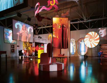 installtion artwork consisting of different shaped screens hanging from the ceiling, pieces of set, wall hung photographs, sculptures and signage.