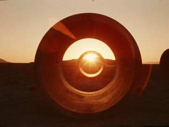 A photograph looking through two large concrete tunnels in the desert with the sun shining through.