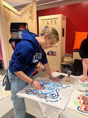 A young person is standing whilst drawing at a table.