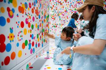 Woman kneeling down next to a child touching a wall covered in colourful dots.