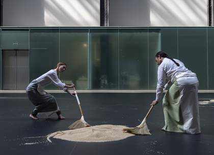 two performers sweeping rice on a dark floor