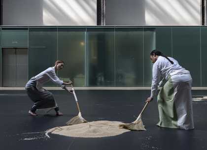 two performers sweeping rice on a dark floor