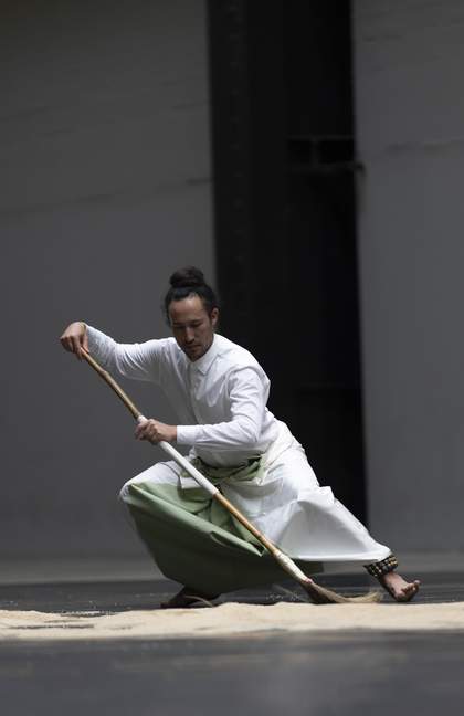 performer crouching while holding a broom