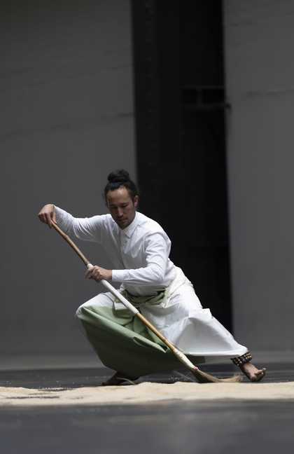 performer crouching while holding a broom