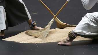 close up of performers' feet with bells on a dark surface scattered with rice