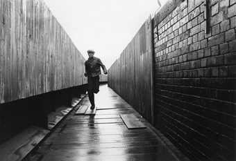 Black and white image of a man running down an alleyway