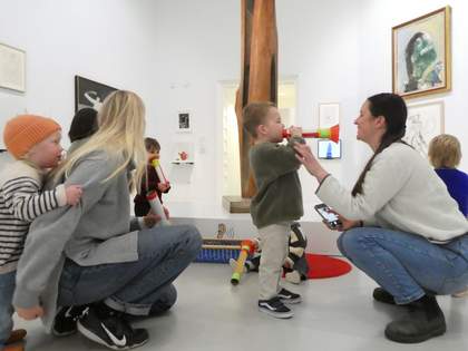 A group of adults and small children playing with colourful toys in an art gallery space.