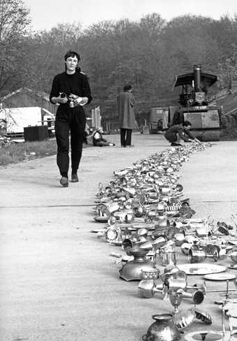 Photograph of Cornelia Parker with silver objects and a steamroller in the background