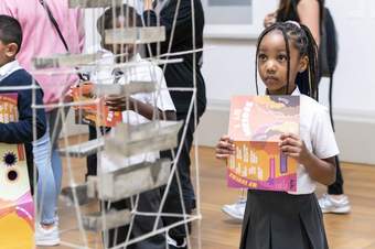 A child holding a colourful leaflet looking at a sculpture