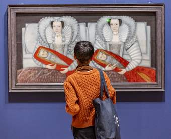 A person in an orange jumper looking at a painting framed on a bright blue gallery wall