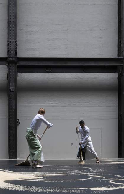 two performers sweeping rice on a dark floor