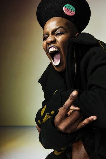 A black queer person wearing black lipstick and dark clothing forming the rock hand gesture with their mouth open wide
