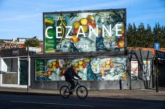 A man cycling in front of a poster for the Cezanne exhibition at Tate