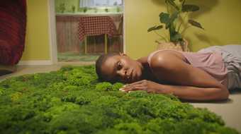 A woman lies on the floor, resting her head on a patch of moss,
