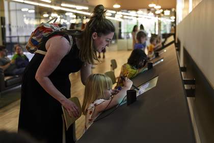 A child drawing on an electronic screen, supervised by an adult