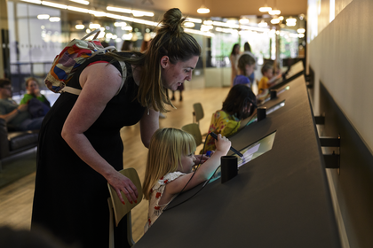 A child drawing on an electronic screen, supervised by an adult