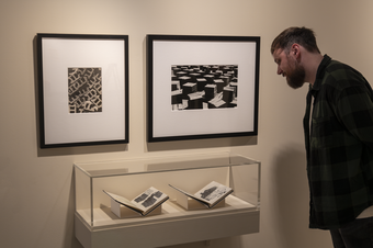 A visitor looking at a display cabinet which contains two sketchbooks. There are two photographs displayed on the wall above.