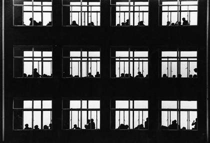 A photograph of a building with lit windows and people inside.