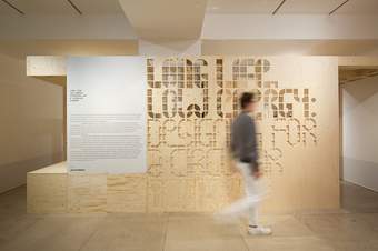 A photograph of a visitor walking through an exhibition which says 'Long Life, Low Energy' on a wooden wall.