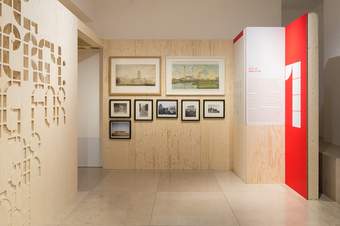 A photograph of an exhibition which features drawings and photographs on the wall.
