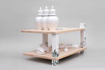 Three white porcelain vessels on a table like structure with three wooden legs painted white with fern patterns and a lower lever with lumps of white porcelain