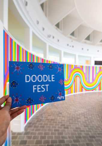 Hand holding a Doodle Fest card against a colourful background.