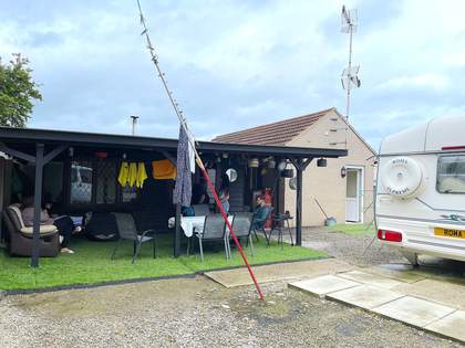 A photograph of a building with a sheltered seating area outside and people sat underneath it