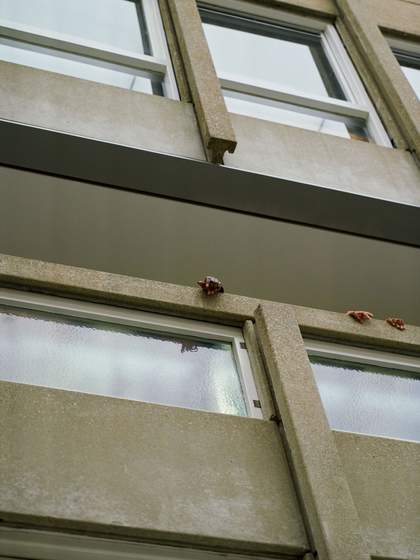 Photograph taken from below of concrete and glass balustrade with 3 hands resting on top