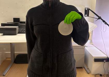 A person holding a breast implant up to their breast.